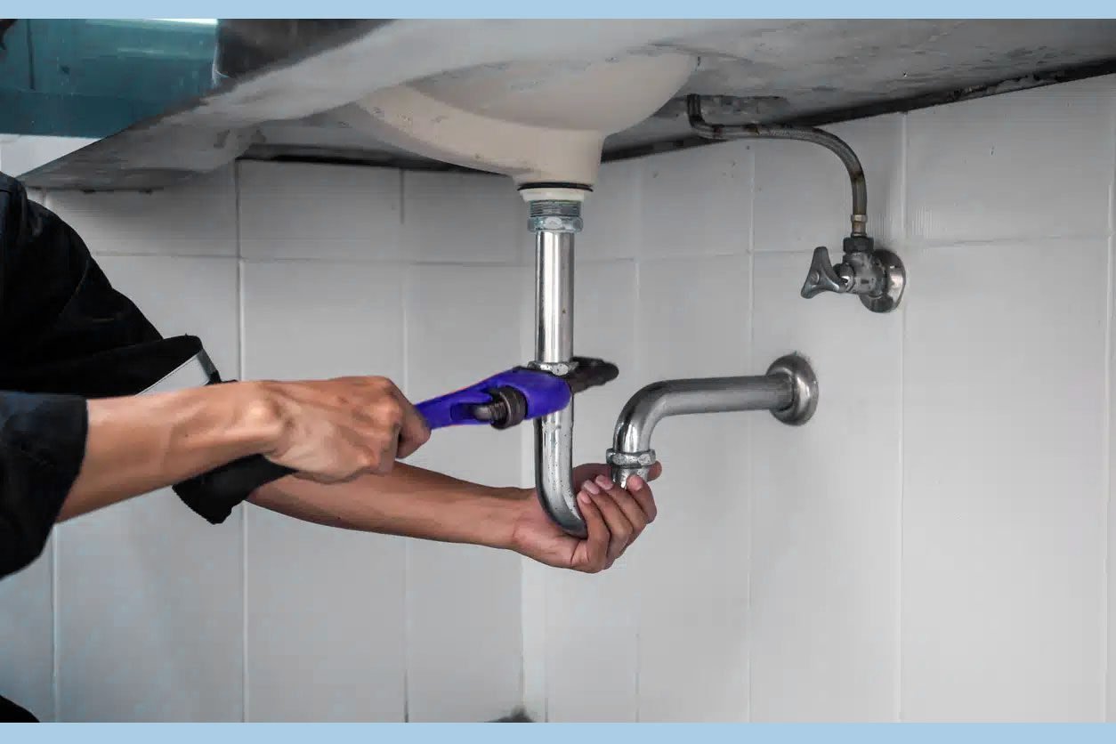 Plombier effectuant un entretien préventif sous un évier, services de maintenance par Desrech Fabbio Plombier Paris 19.